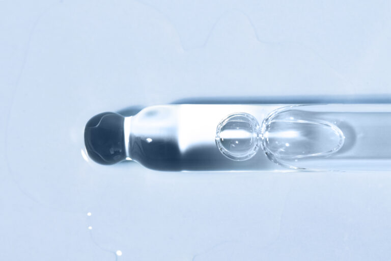 Cosmetic product liquid in a glass dropper on a blue background flat lay. Peptide, serum